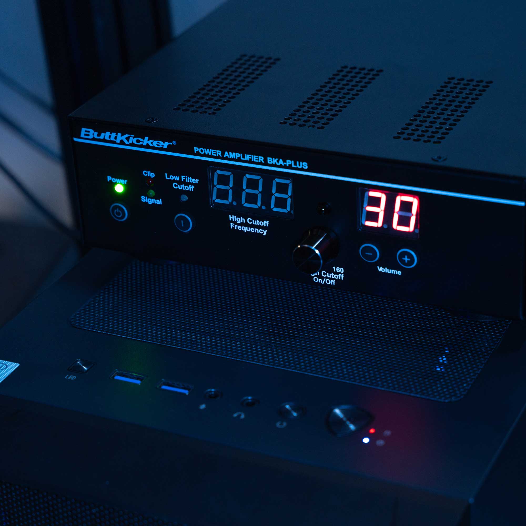 ButtKicker Gamer Plus amplifier with digital display and wireless remote in a sim racing setup