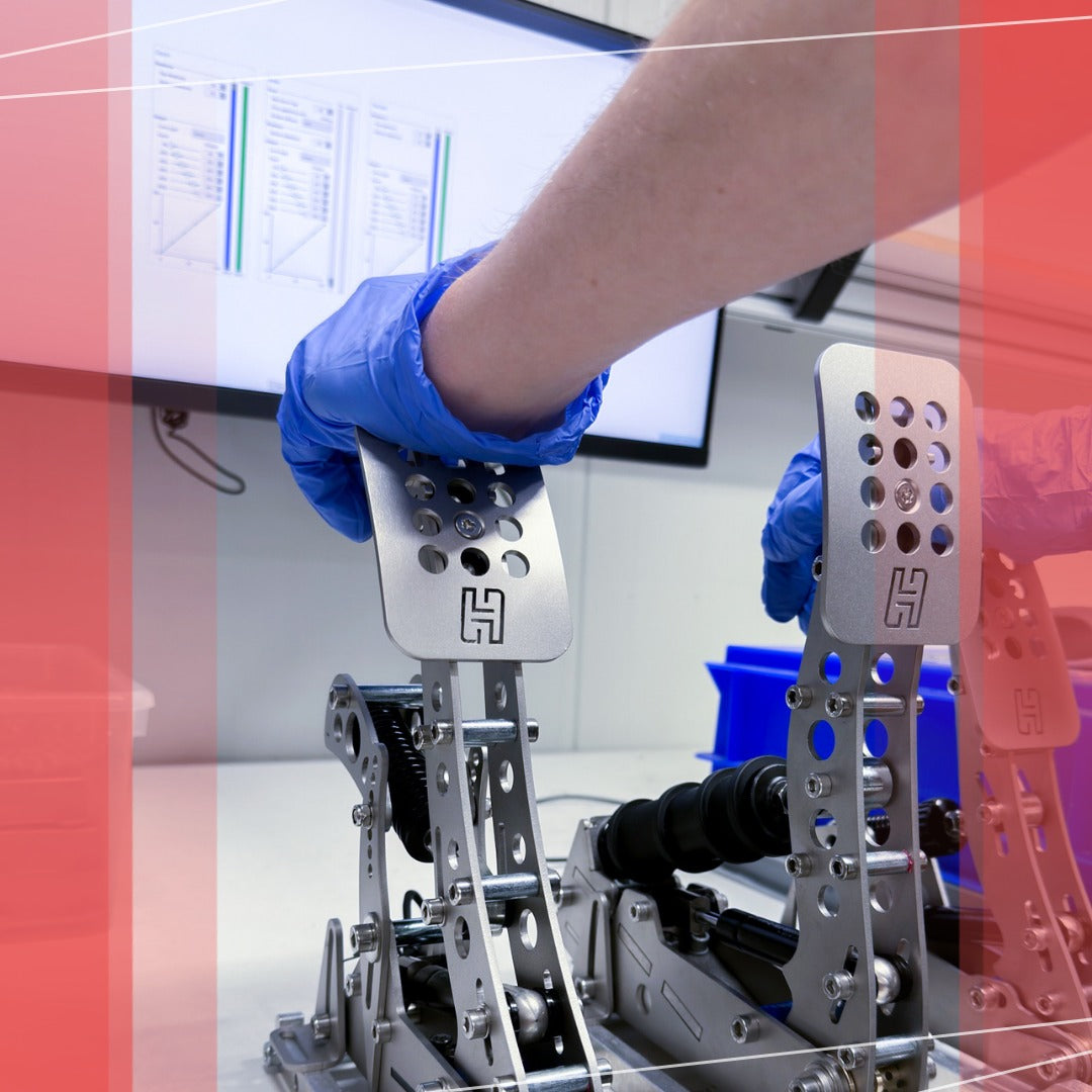Close-up of a person's hand in a glove adjusting metal racing pedals in a tech lab with a screen displaying data in the background.