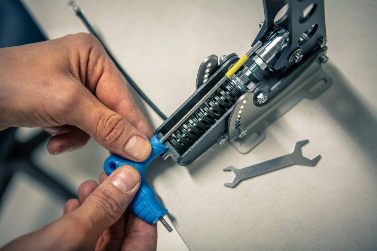Person using a blue screwdriver on a machine component next to a metal wrench on a workbench.