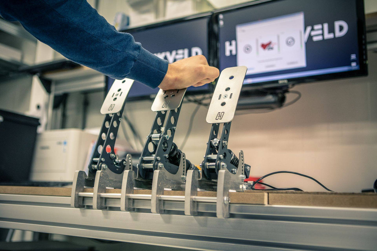 Adjusting racing simulator pedal setup with computers in the background.